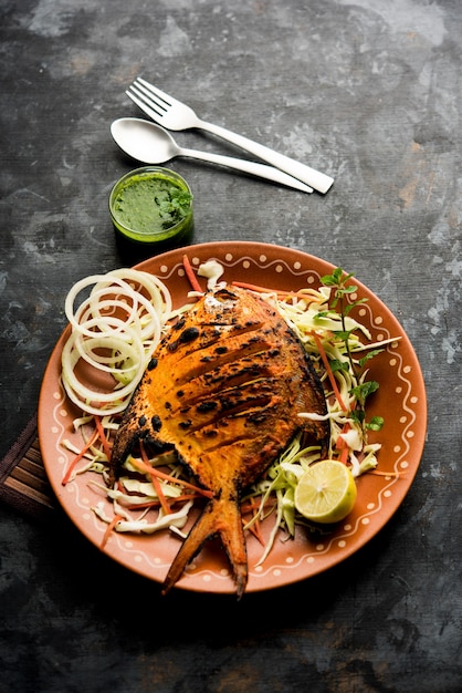 Tandoori Pomfret fish cooked in a clay oven and garnished with lemon , mint, cabbage and carrot salad