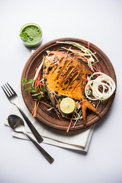 Tandoori Pomfret vis gekookt in een klei-oven en gegarneerd met citroen, munt, kool en wortelsalade