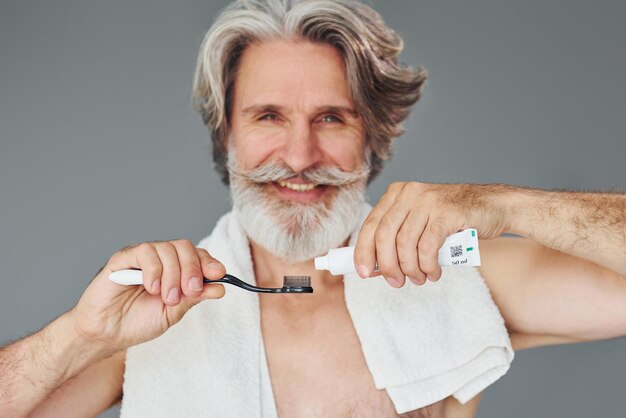 Tandpasta gebruiken Stijlvolle moderne senior man met grijs haar en baard is binnenshuis