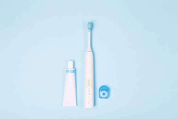 Tandpasta in buis, zijde en tandenborstel op lichtblauwe achtergrond. Kopieer ruimte.