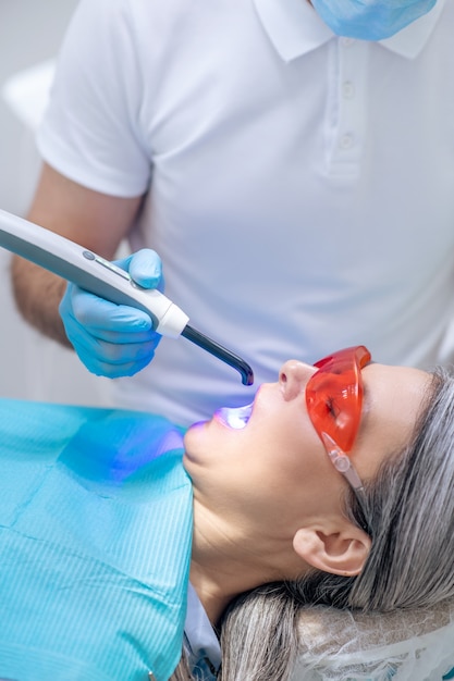 Tandvulling. Vrouw in beschermende brillen met een tandheelkundige restauratie op het kantoor van de tandarts dentist