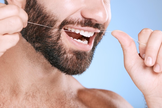 Tandzijde en mondhygiëne met een man in de studio op een blauwe achtergrond die zijn tanden schoonmaakt voor gezond tandvlees Tandartsgezondheidszorg en mond met een jonge man flossen om pest of gingivitis te verwijderen