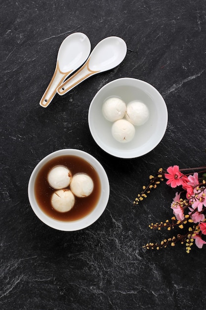 Tang Yuan, 중국 찹쌀 만두 공, 설탕 생강 또는 야자 설탕 시럽을 동지 신년 축제 음식을 위해 검은색 바탕에 붉은 중국식으로 얹습니다.