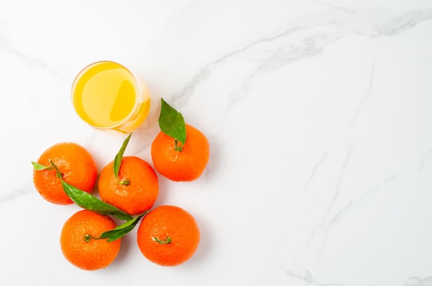 Tangerine, clementine with leaves on and a glass of orange juice with white background. Top view.