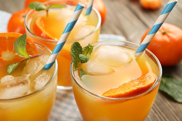 Tangerine cocktails with ice mint and straws served on a wooden table close up