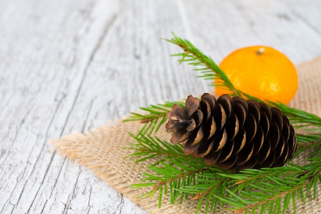 Photo tangerine and fir tree branch with cone on jute napkin