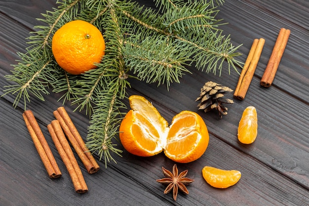 Tangerine halves and cinnamon sticks. Pine branches and cones. Flat lay. Dark wooden background.