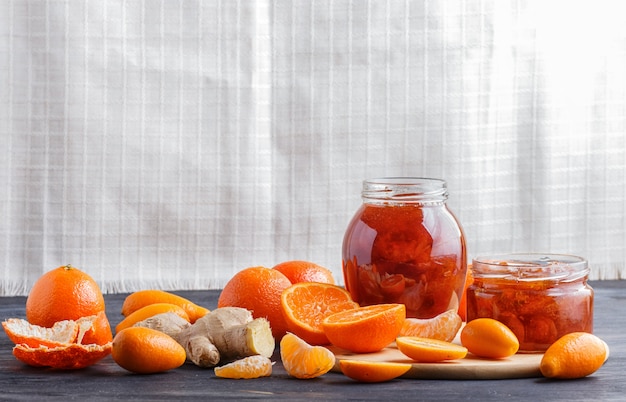 Marmellata di mandarino e kumquat in un vaso di vetro su un tavolo in legno nero e sfondo di lino bianco.