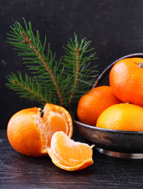 Tangerine in a metal basket with a branch of a Christmas tree on a black background