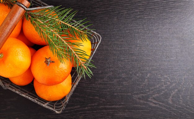 Mandarino in un cesto di metallo con un ramo di un albero di natale su uno sfondo nero