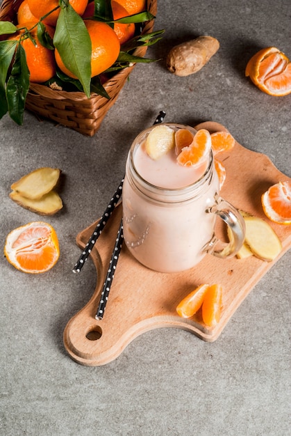 Tangerine Smoothie met Gember in mason jar, met verse rauwe mandarijnen, in grijze steen achtergrond bovenaanzicht kopie ruimte