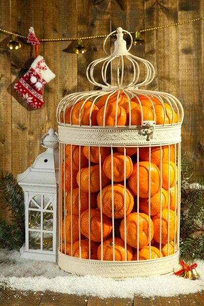 Tangerines in decorative cage with Christmas decor, on wooden background