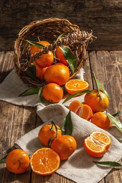 Tangerines falling out of the basket. Oranges, mandarins, clementines, citrus fruits) with green leaves. Wooden background, rustic style, close up