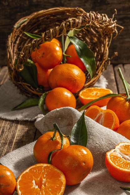 Tangerines falling out of the basket. Oranges, mandarins, clementines, citrus fruits) with green leaves. Wooden background, rustic style, close up