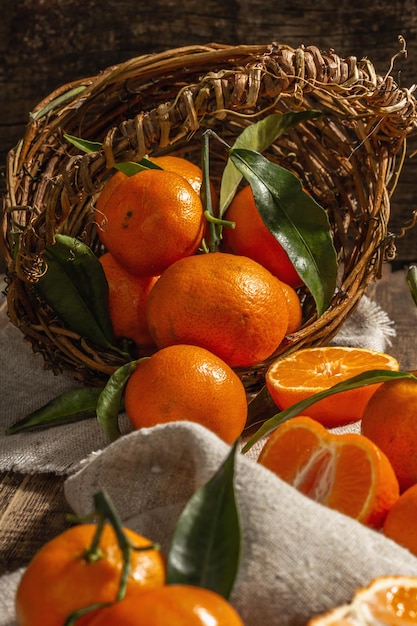 Tangerines falling out of the basket. Oranges, mandarins, clementines, citrus fruits) with green leaves. Wooden background, rustic style, close up