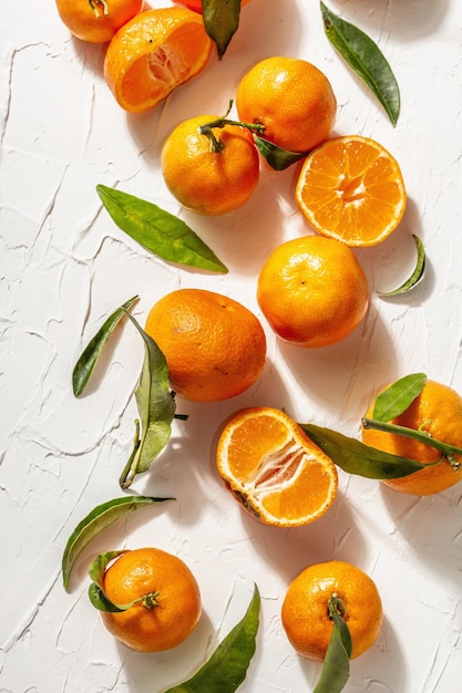 Tangerines (oranges, mandarins, clementines, citrus fruits) with green leaves. Modern hard light, dark shadow. White putty background, creative flat lay, top view