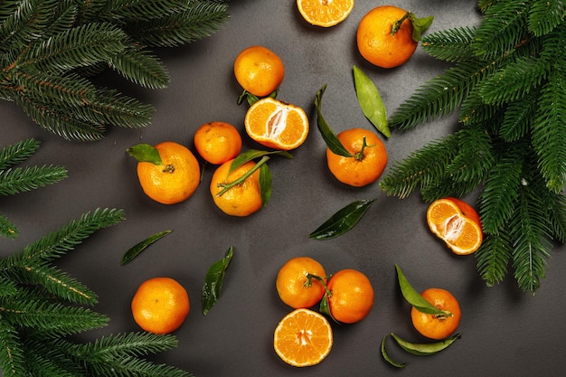 Tangerines (oranges, mandarins, clementines, citrus fruits) with leaves and fir tree branches. Black stone background, festive flat lay, top view