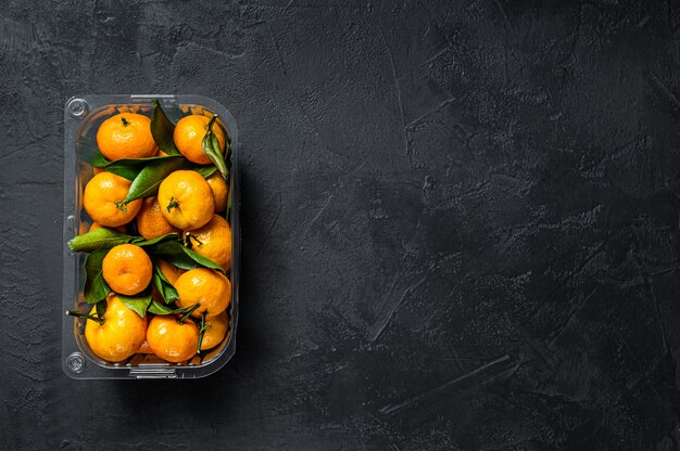 Tangerines in a plastic container from the supermarket. Black background. Top view. Space for text