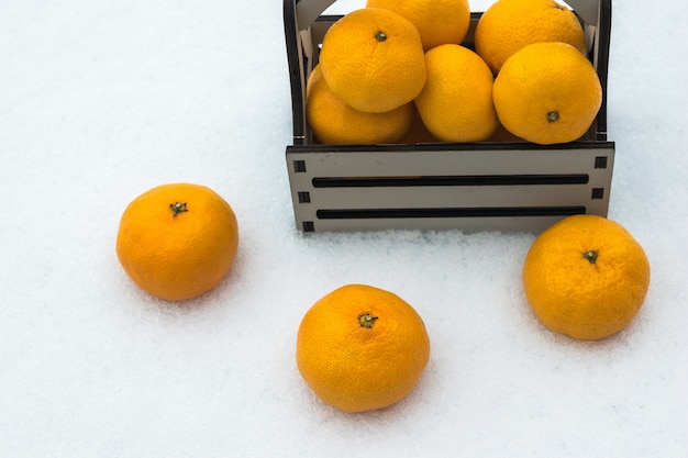 Tangerines scattered in the snow and a wooden box. Popular citrus fruits.