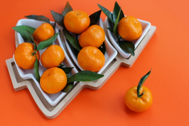 Tangerines in the shape of a Christmas tree on an orange background. Christmas food background, top view. A fun edible Christmas tree