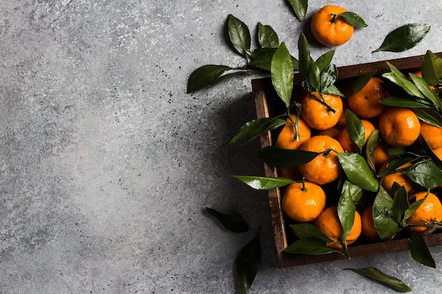 Tangerines with green leaves in wooden box on light background