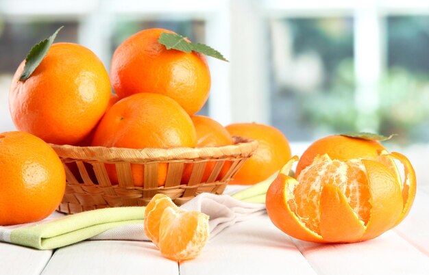 Tangerines with leaves in a beautiful basket on wooden table on window background