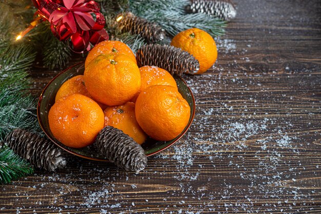 Tangerines on a wooden table with branches of a Christmas tree and pine cones covered with snow.