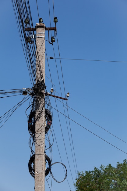 Tangled electric cables on concrete post Blue sky selective focus vertical orientation