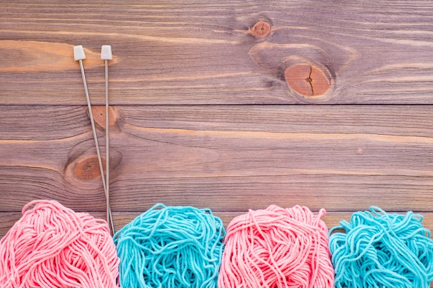 Tangles of pink and mint yarn and needles on a wooden table.