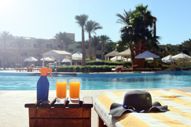 Succhi di lozione abbronzante sul tavolo da spiaggia con un cappello di paglia blu vicino alla piscina del resort