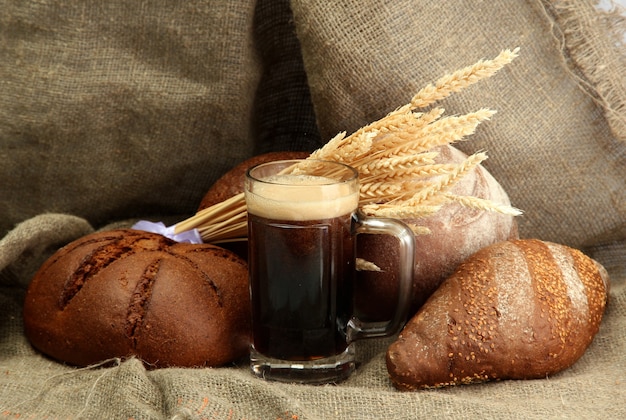 Tankard of kvass and rye breads with ears, on burlap background