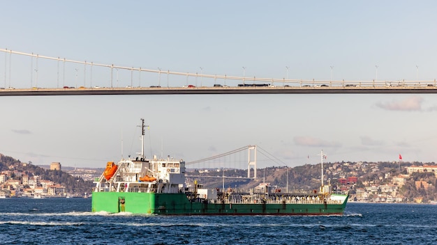 Танкерный корабль проходит через Босфор с Босфорским мостом в Стамбуле, Турция, или турецкий пролив Босфор, соединяющий Европу с Азией Танкерный корабль в Стамбуле, Турция