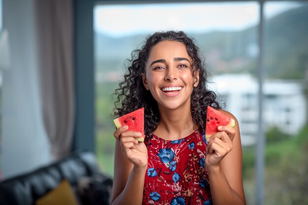 Tanned brunette enjoys fresh red watermelon in her hands