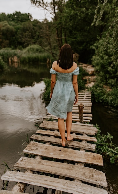 A tanned brunette girl walks across the river alone an old wooden bridge