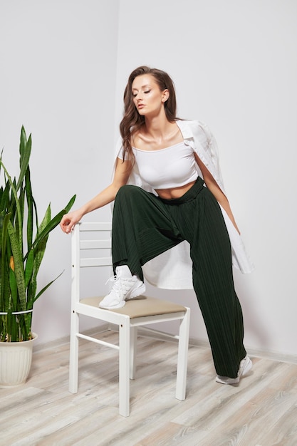 Tanned darkhaired girl in stylish clothes holds her leg on a chair