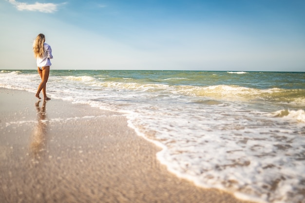 A tanned girl in a blue swimsuit and a light shirt enjoys the summer at the seaside