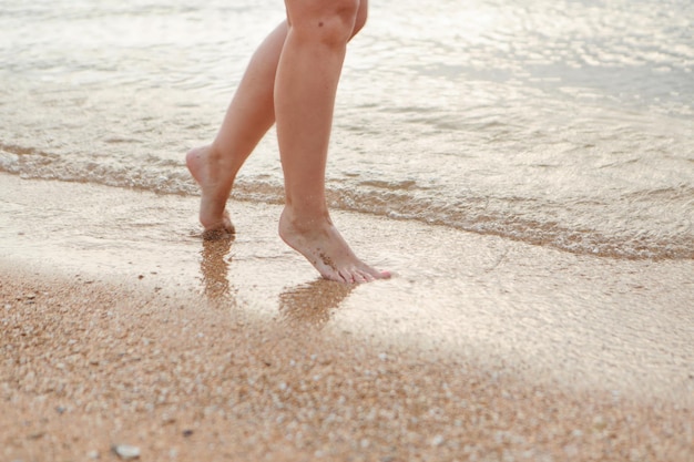 Tanned legs in the sand closeup a wave rolls onto the sand summer vacation by the sea