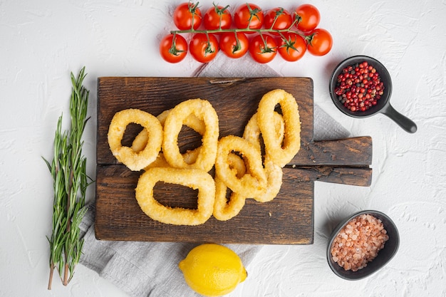 Foto tapa di calamari in pastella affettati in anelli, su tavola di servizio, su sfondo di tavolo in pietra bianca, vista dall'alto piatta