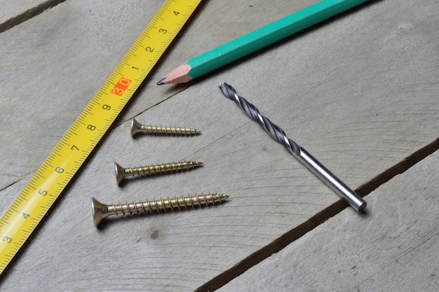 tape measure, pencil and screws with a drill lie on a wooden background. close-up.