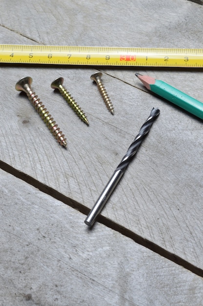 tape measure, pencil and screws with a drill lie on a wooden background. close-up.