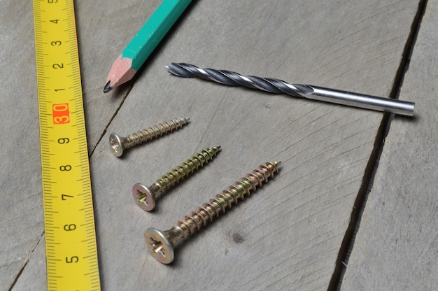 Tape measure, pencil and screws with a drill lie on a wooden background. close-up.