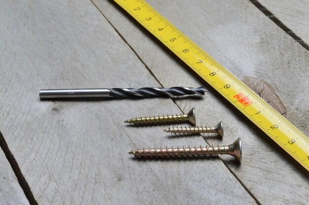 tape measure, screws and a drill lie on a wooden background. close-up.