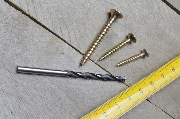 Tape measure, screws and a drill lie on a wooden background. close-up.