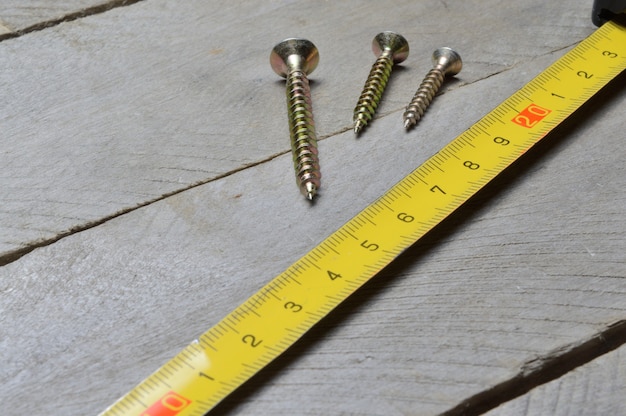 Tape measure and screws lie on a wooden background. close-up.