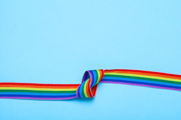 Tape met een knoop. LGBT Pride Rainbow Ribbon tegen blauwe achtergrond.