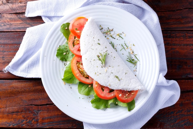 Tapioca of beiju met groenten, tomaat, rucola in witte plaat over rustieke houten tafel Veganistisch fitnessvoedsel glutenvrij