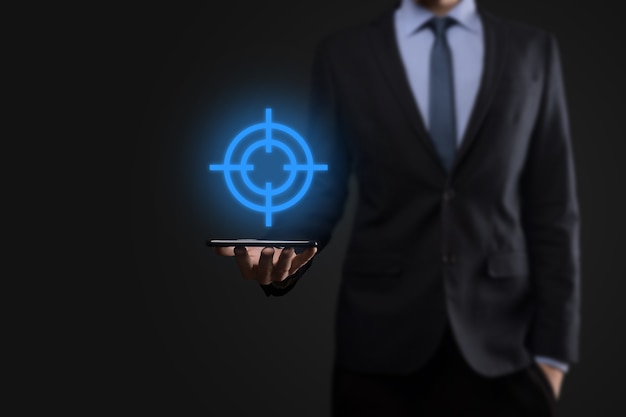 Photo targeting concept with businessman hand holding target icon dartboard sketch on chalkboard. objective target and investment goal concept.