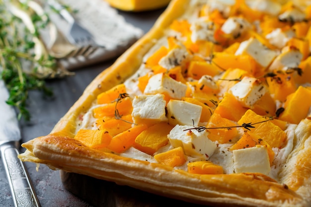 Tart with pumpkin, feta, ricotta cheese and thyme on a dark concrete background. 