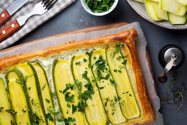 Tart with zucchini, ricotta cheese and parsley on a dark concrete surface