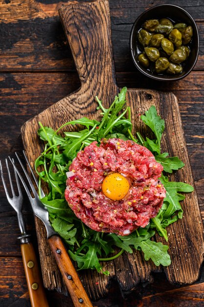 Tartaar rundvlees met een kwartelei en rucola geserveerd op een snijplank.